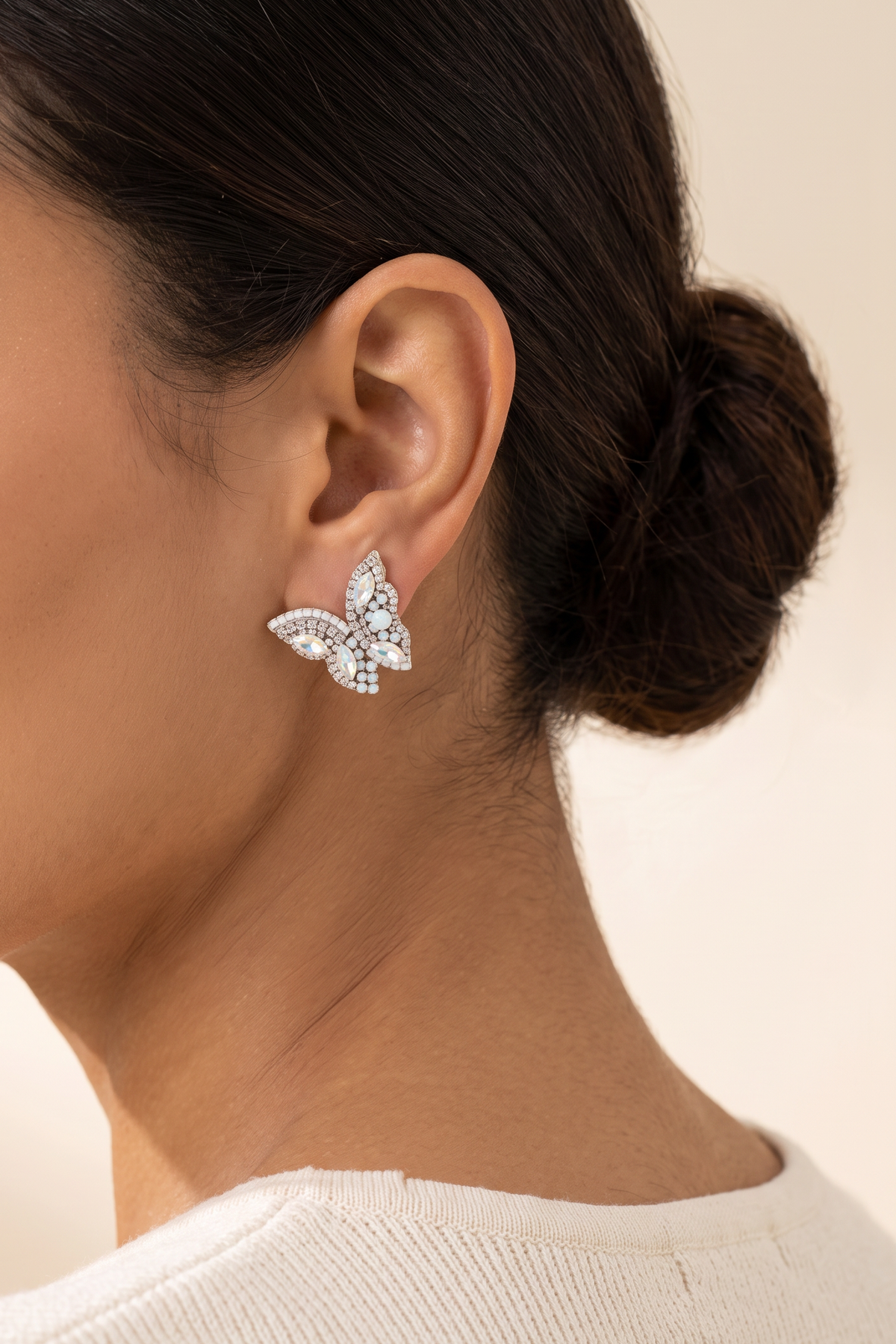 June Butterfly Earrings in White worn on the earlobe at true size: a small half-butterfly stud about 1 in across