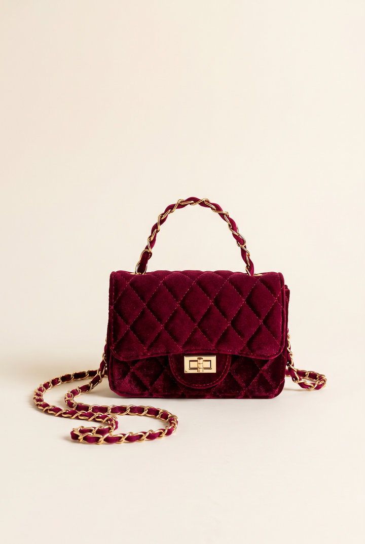 Burgundy quilted velvet shoulder bag standing on a plain studio background