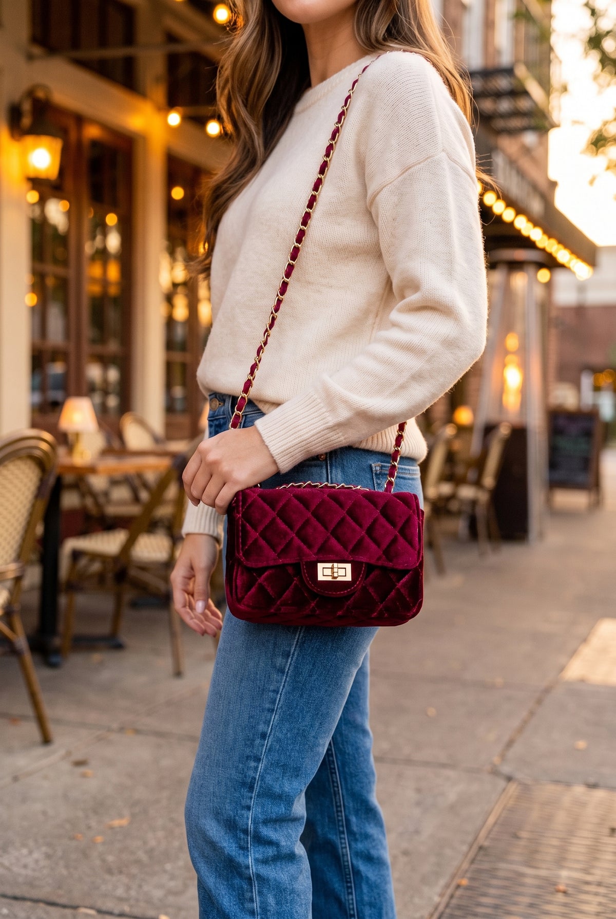 Burgundy velvet bag worn on the shoulder with a cream sweater and jeans