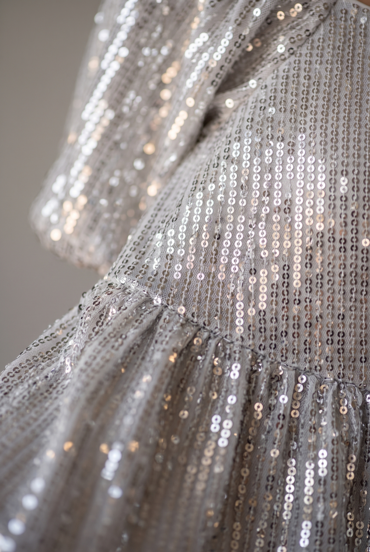 Close-up of the silver sequin dress fabric: rows of small sequins, the puff sleeve edge and the empire seam.