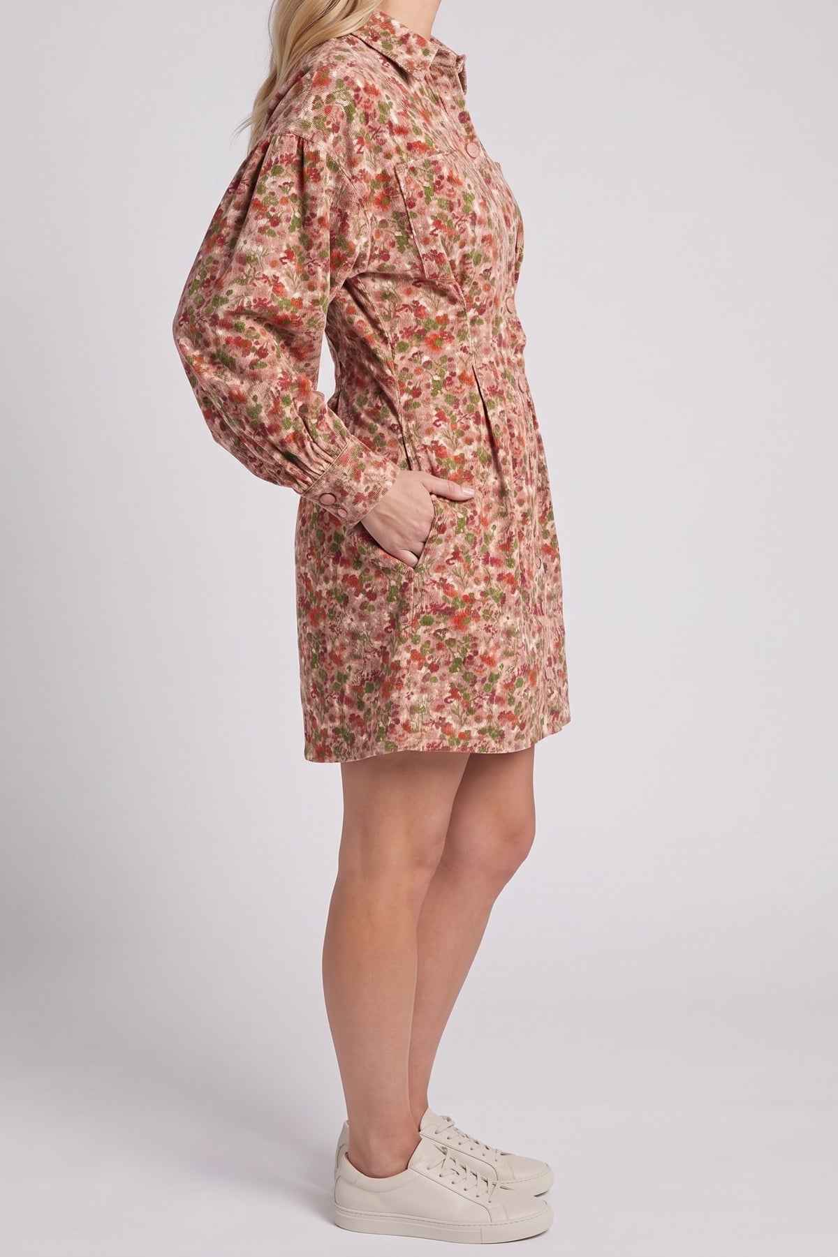 Side view of the floral corduroy shirt dress showing the balloon sleeve, pleated waist, side pocket and mid-thigh length.