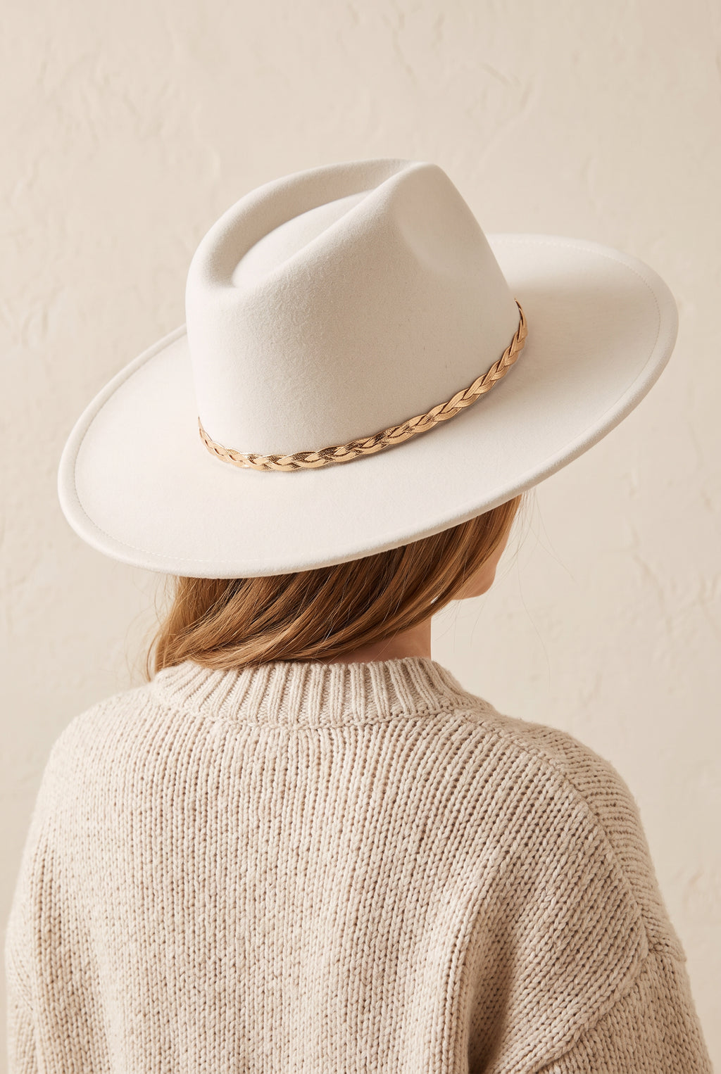 Hadley ivory felt fedora with a braided gold chain band, worn, seen from behind over a cream knit sweater