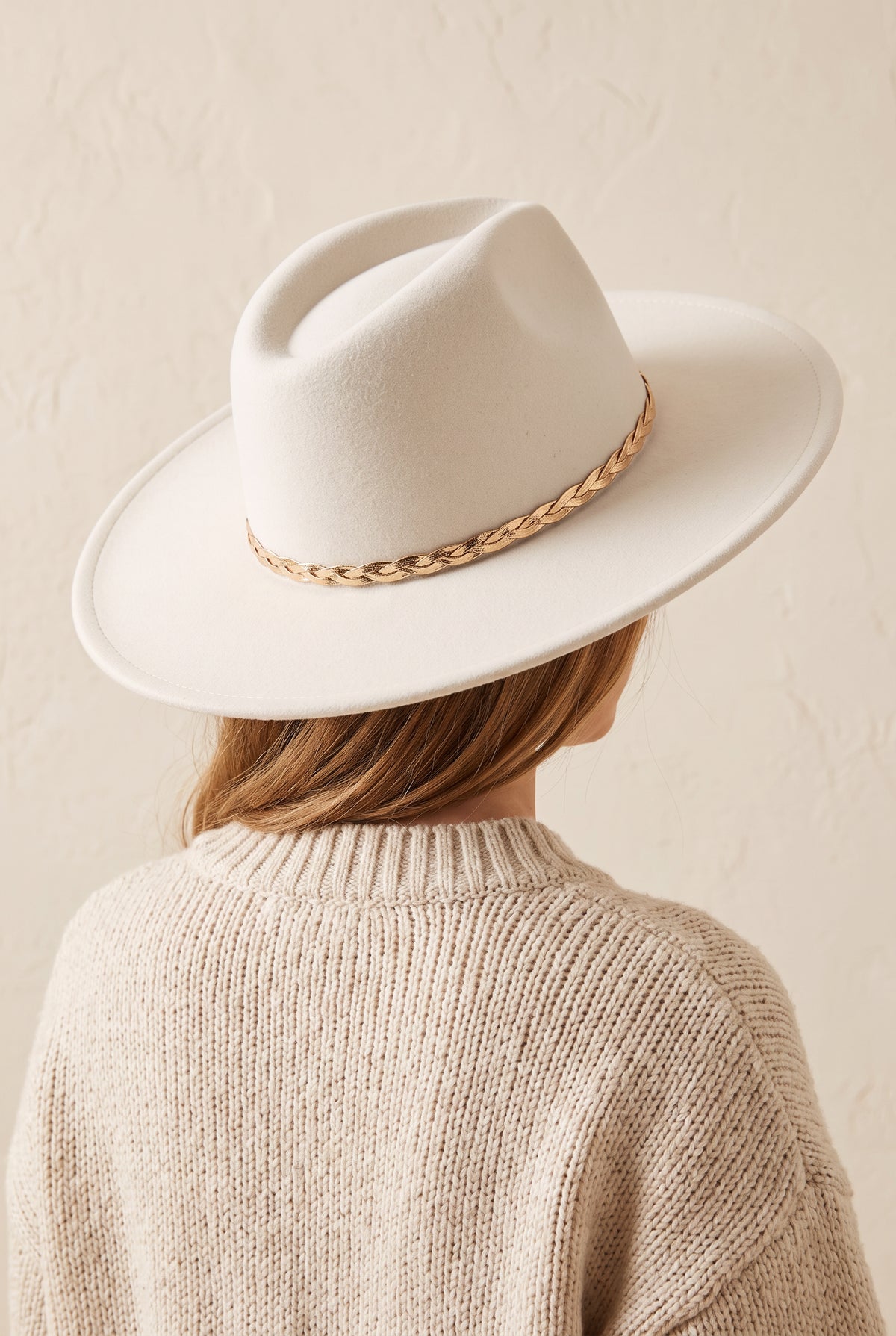 Hadley ivory felt fedora with a braided gold chain band, worn, seen from behind over a cream knit sweater