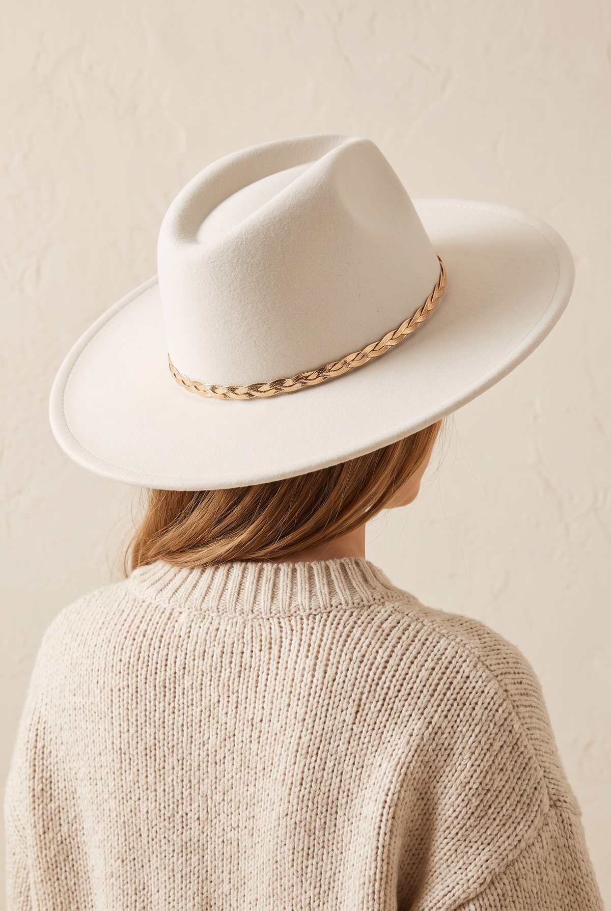 Hadley ivory felt fedora with a braided gold chain band, worn, seen from behind over a cream knit sweater