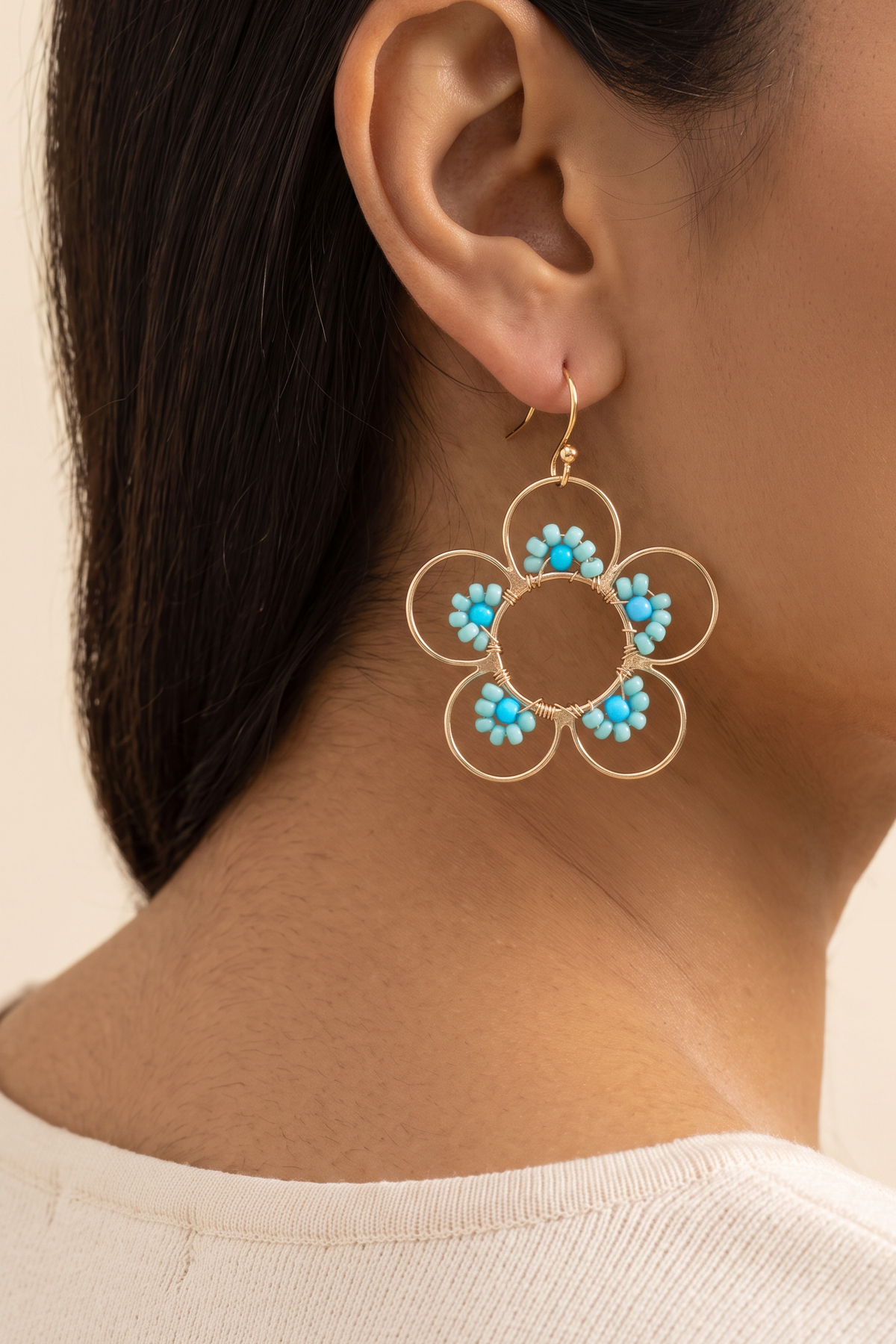 Daisy Earrings in Blue worn on the ear at true size: open gold wire flower about 4 cm across with turquoise seed beads