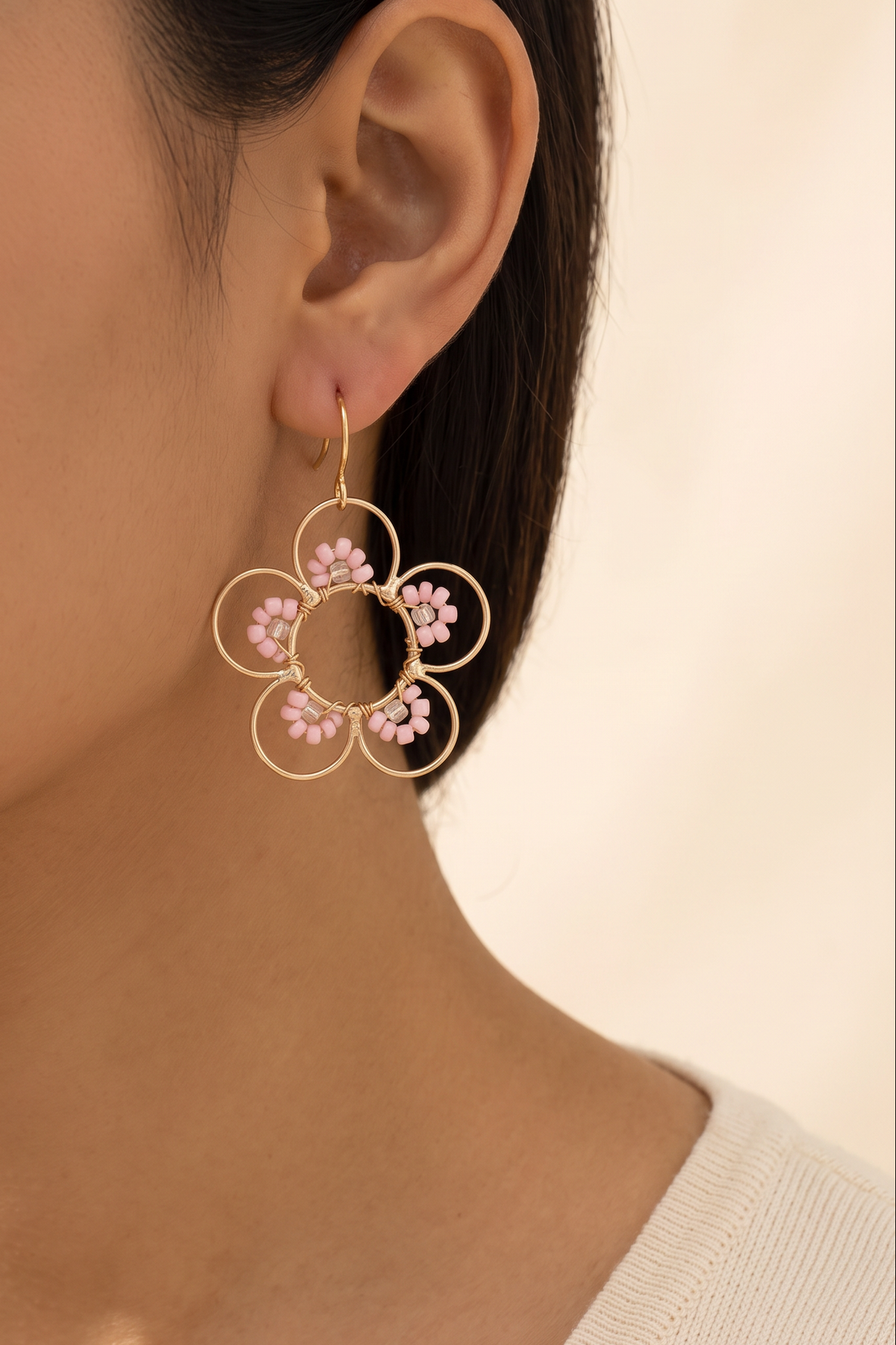 Daisy Earrings in Light Pink worn on the ear at true size: open gold wire flower about 4 cm across with pale pink seed beads