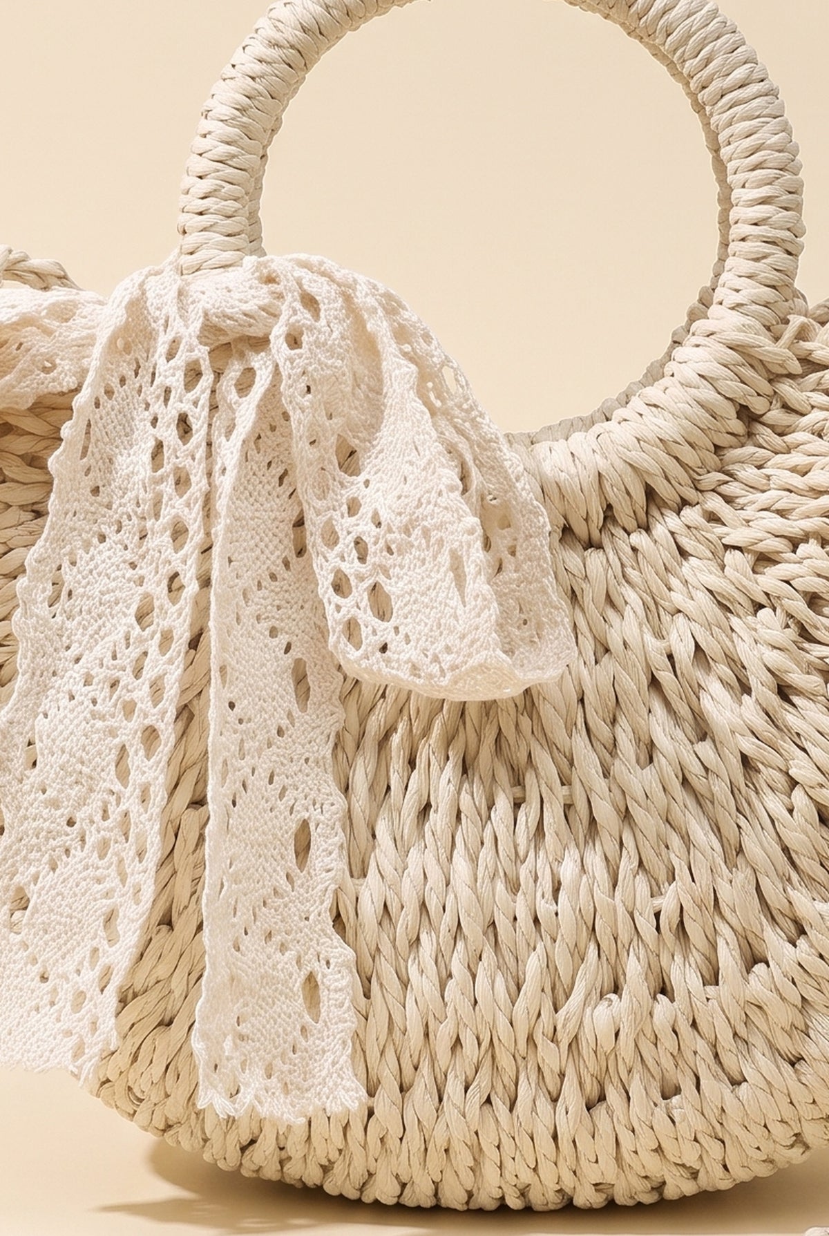 Close-up of the Beige Rose bag: crochet lace bow tied at the round straw ring handle and the twisted paper straw weave