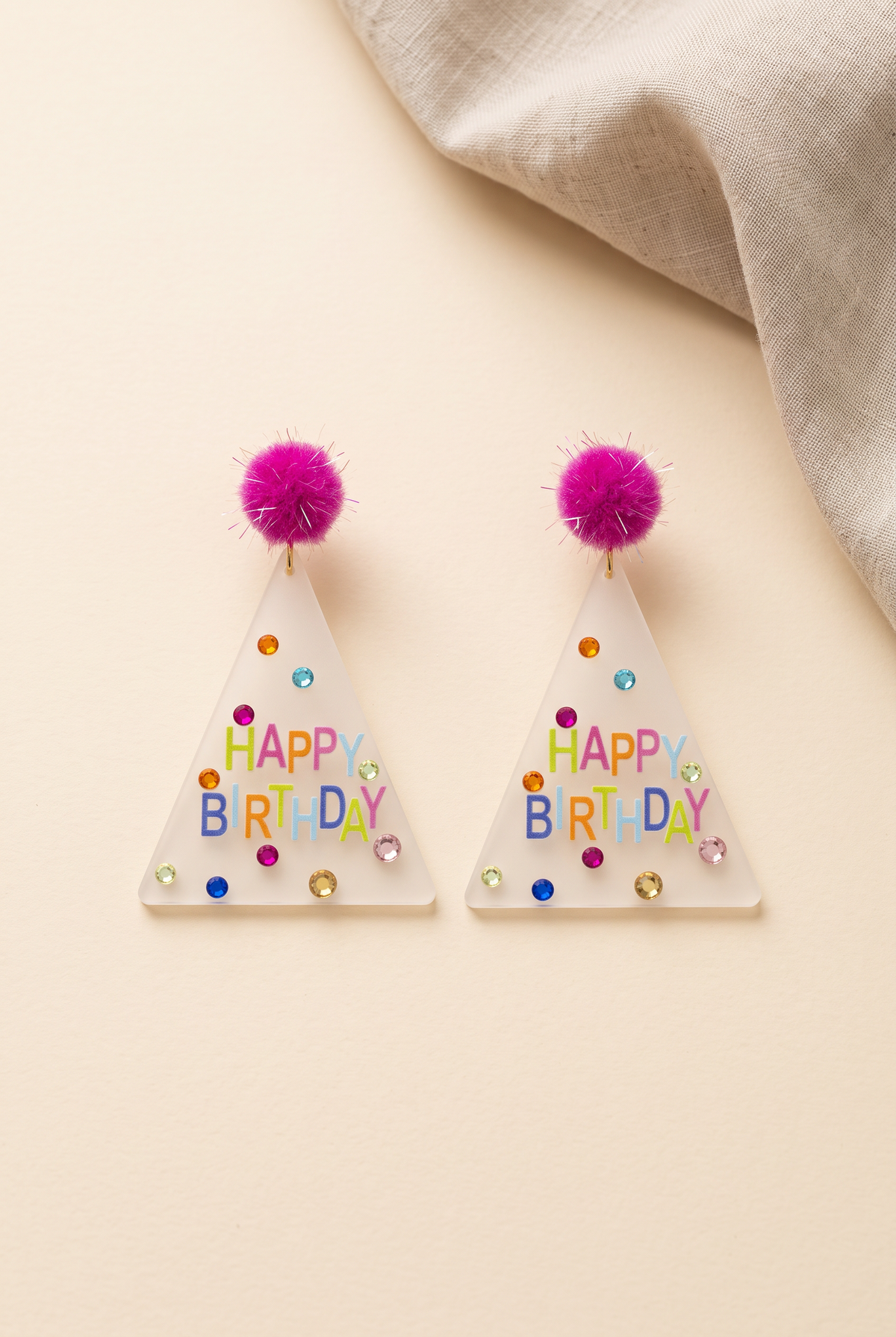 Dorothy Make A Wish Earrings: pair of frosted acrylic party hat earrings with hot pink pom-pom studs, multicolour HAPPY BIRTHDAY print and rhinestone confetti, on cream