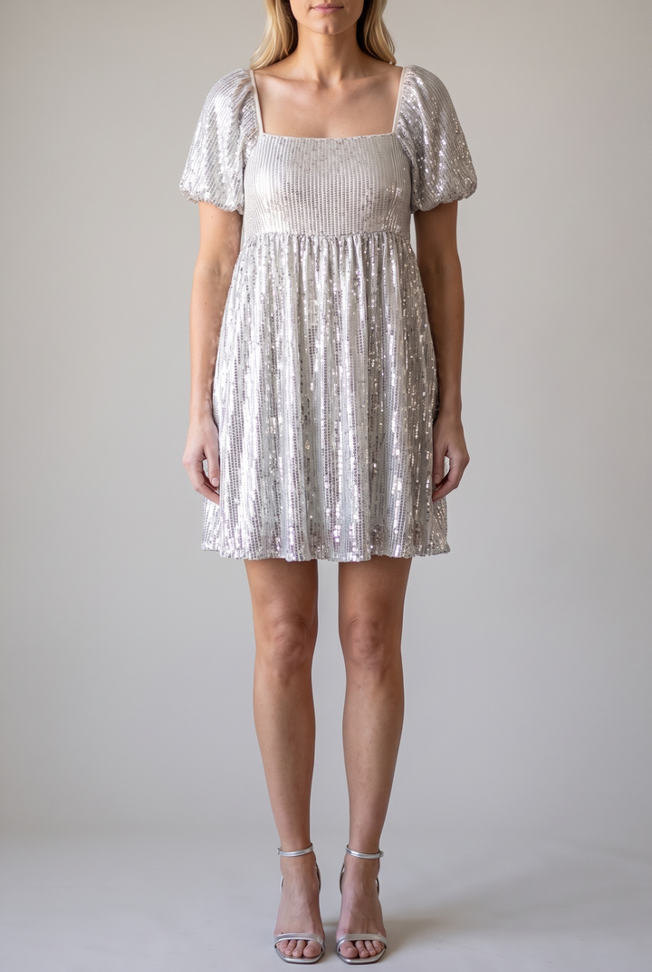 Front view of the silver sequin babydoll mini dress with square neckline, puff sleeves and empire waist, on a light-grey studio backdrop.