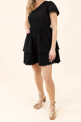 Front of the Flirty Noir Fantasy black one-shoulder mini dress, showing the scalloped asymmetric neckline, puff sleeve and two scalloped tiers