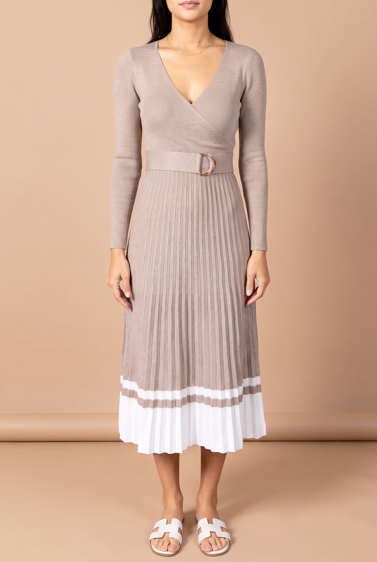 Front view of the I've Loved You For So Long pleated sweater dress in taupe rib knit with the belted waist and white striped pleated hem, on a beige studio backdrop.