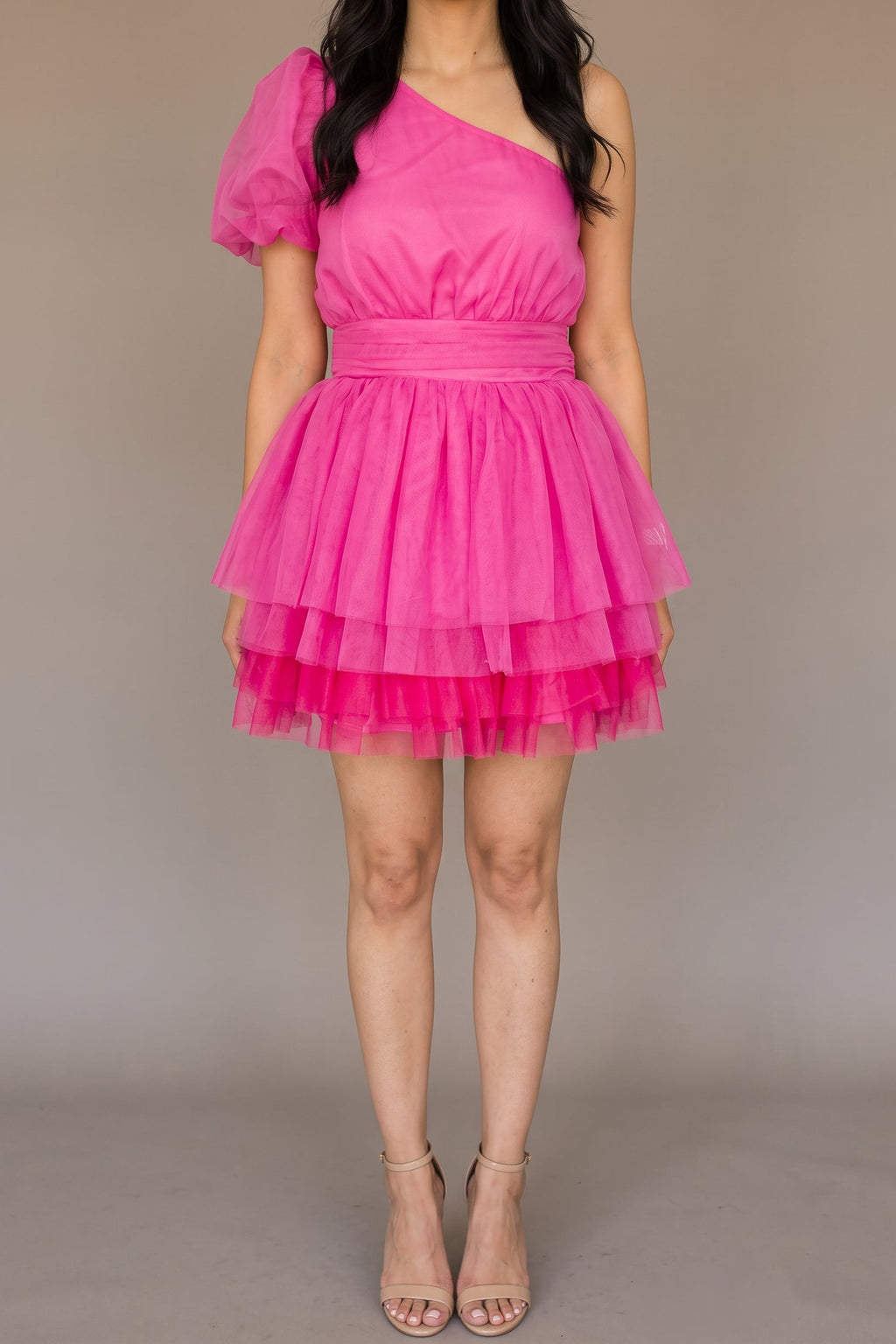 Front of the See You Again hot pink mini dress, showing the one-shoulder neckline, single sheer puff sleeve, wide pleated waistband and layered tulle skirt at mid-thigh