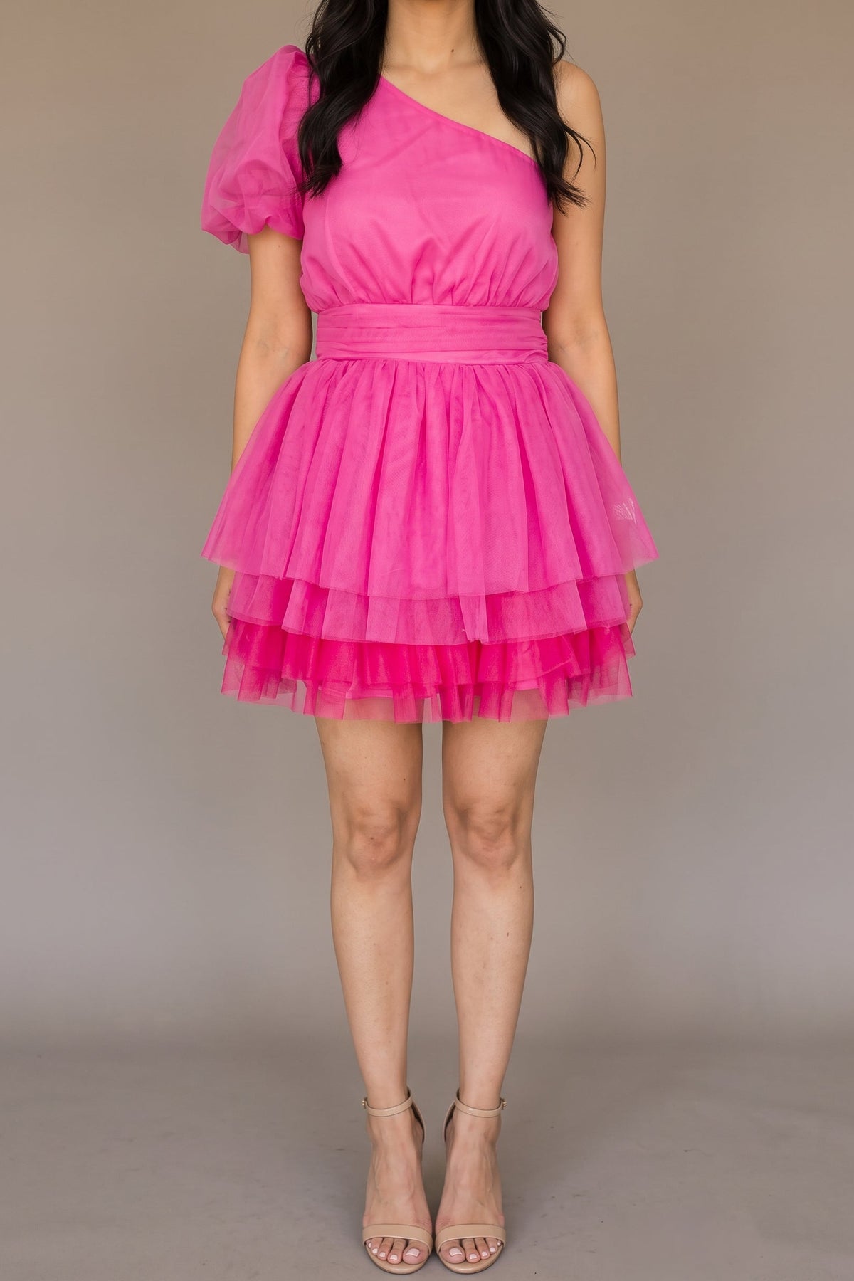 Front of the See You Again hot pink mini dress, showing the one-shoulder neckline, single sheer puff sleeve, wide pleated waistband and layered tulle skirt at mid-thigh