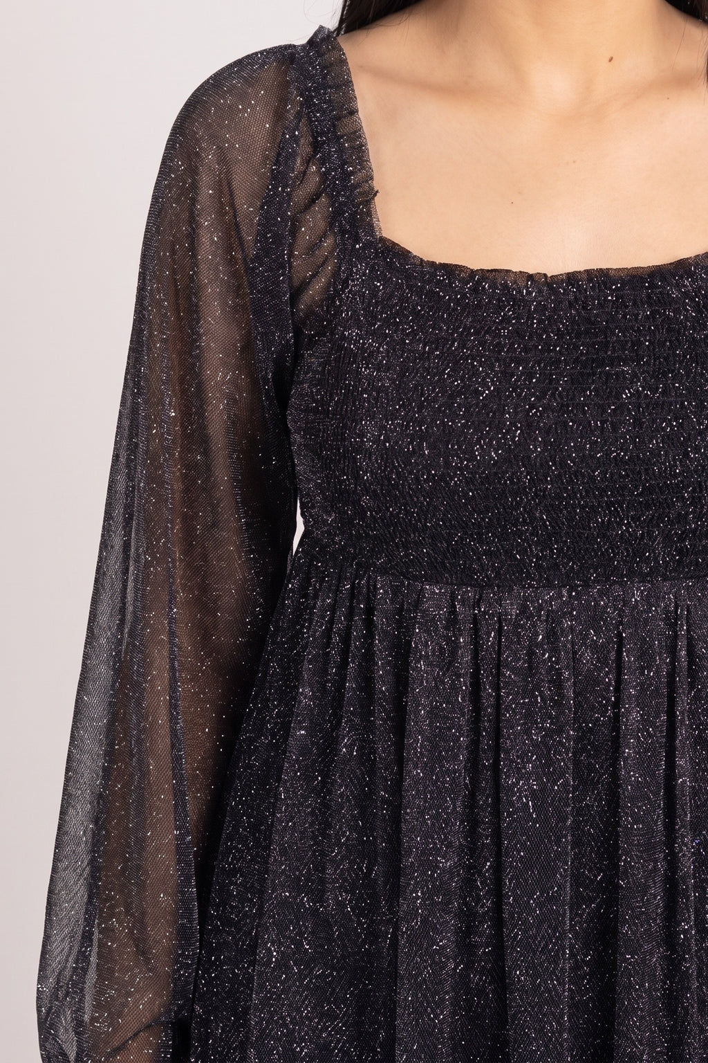 Close-up of the black glitter mesh with silver sparkle, smocked square neck bodice and sheer long sleeve.