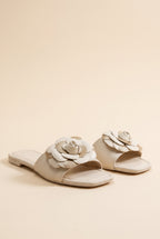 Grace Glitter Flower Accent Sandals, pair of ivory faux leather flat slides with a layered ivory and gold glitter flower on the strap
