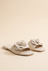 Grace Glitter Flower Accent Sandals, pair of ivory faux leather flat slides with a layered ivory and gold glitter flower on the strap