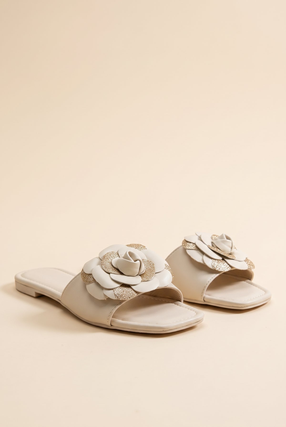 Grace Glitter Flower Accent Sandals, pair of ivory faux leather flat slides with a layered ivory and gold glitter flower on the strap