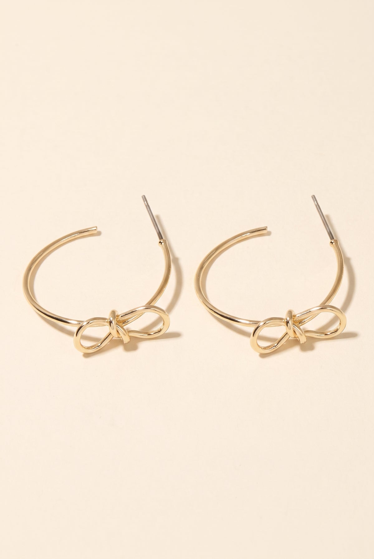 Harley Bow Tie Hoop Earrings: a pair of thin open gold hoops with a post and a sculpted gold wire bow at the front