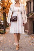 White crochet bodice dress worn with an ivory tweed blazer over the shoulders, tan western ankle boots and a brown quilted chain crossbody on an autumn sidewalk.