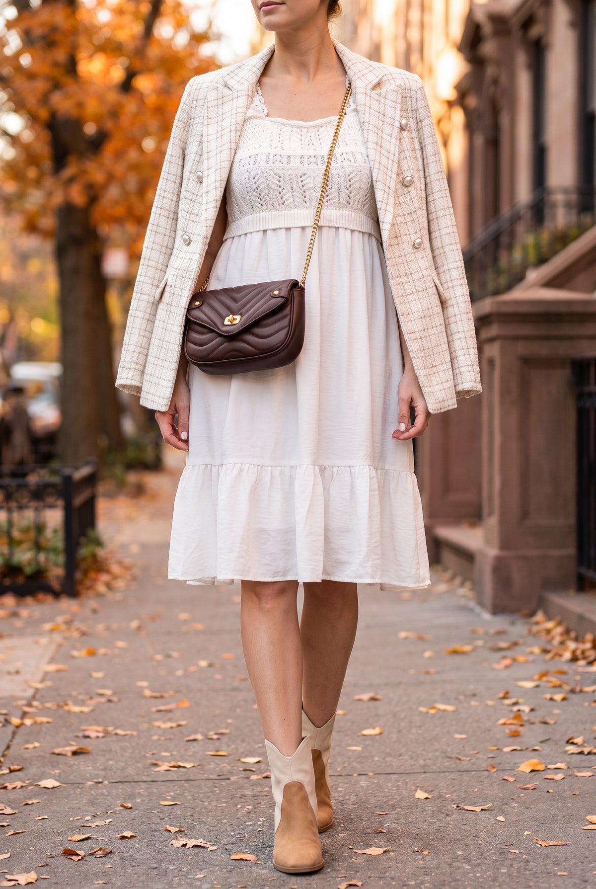 White crochet bodice dress worn with an ivory tweed blazer over the shoulders, tan western ankle boots and a brown quilted chain crossbody on an autumn sidewalk.
