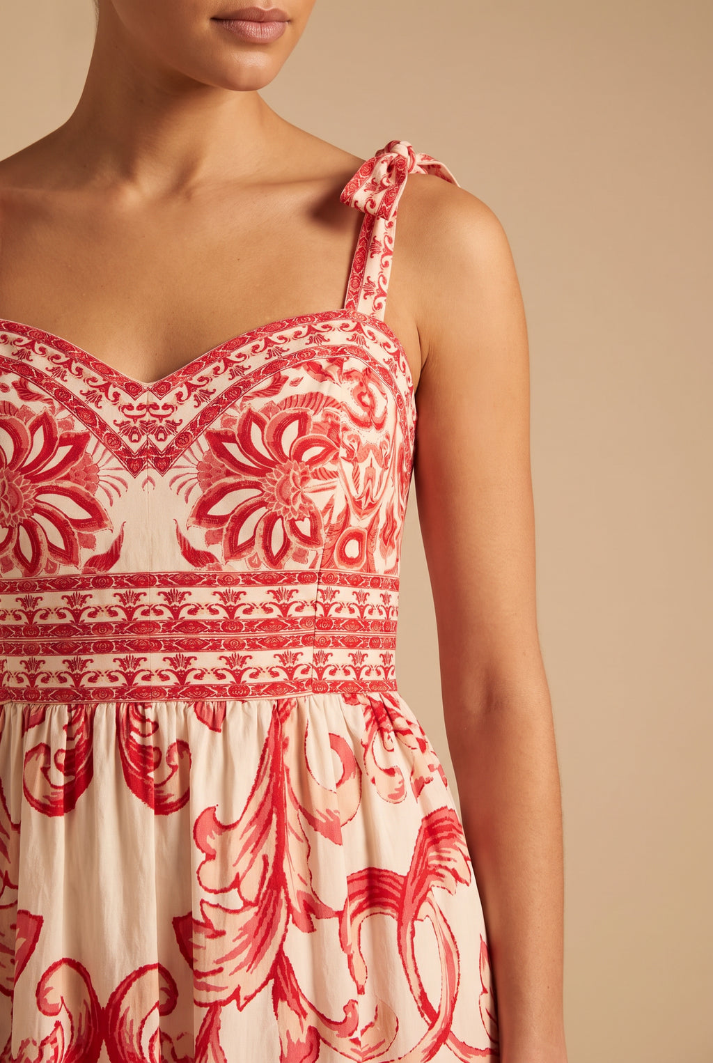 Close-up of the sweetheart neckline, tie strap bow, printed waist border and red scroll print.