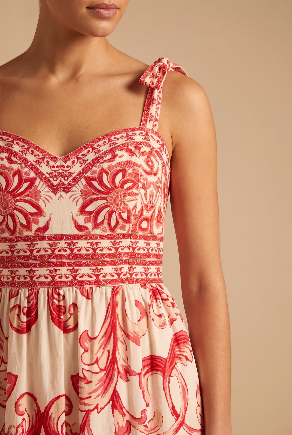 Close-up of the sweetheart neckline, tie strap bow, printed waist border and red scroll print.