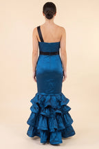 Back view of the blue satin mermaid gown showing the single black shoulder strap, pleated back bodice with zip, black waistband and floor length ruffle tiers.