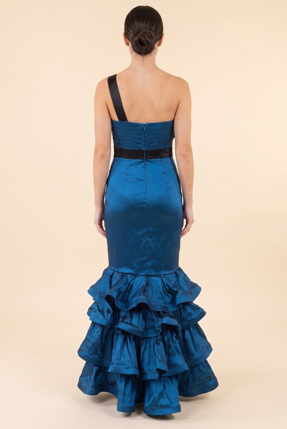 Back view of the blue satin mermaid gown showing the single black shoulder strap, pleated back bodice with zip, black waistband and floor length ruffle tiers.