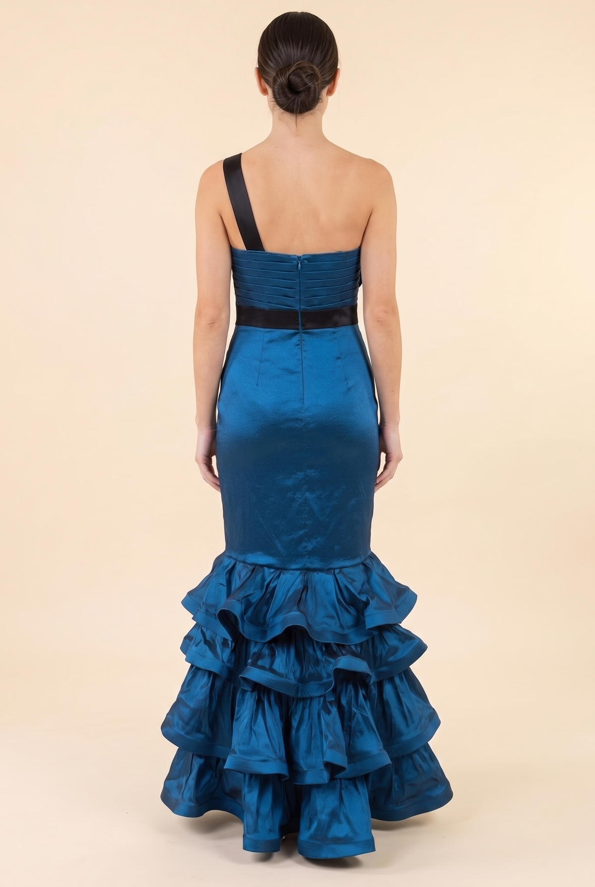 Back view of the blue satin mermaid gown showing the single black shoulder strap, pleated back bodice with zip, black waistband and floor length ruffle tiers.