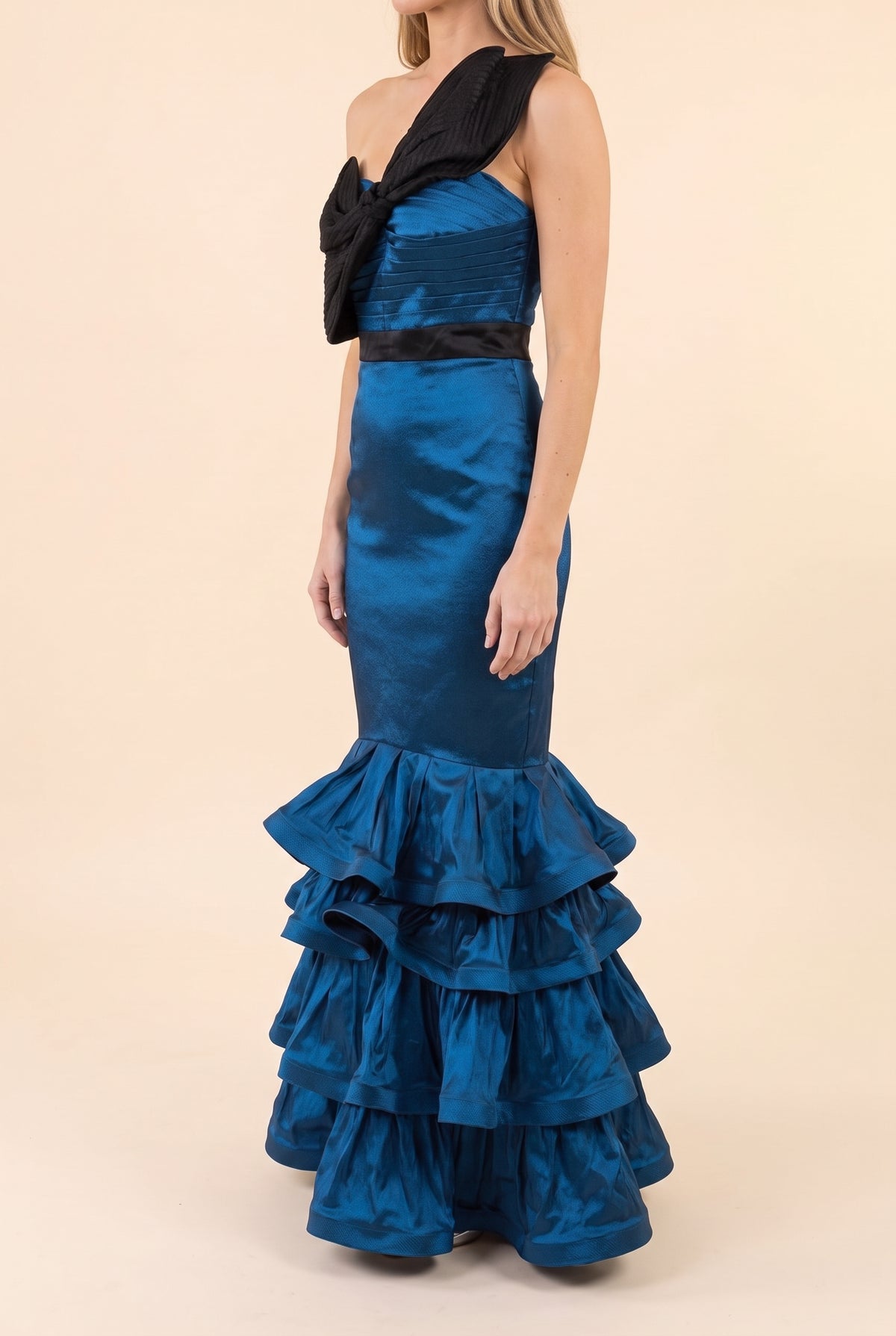 Side view of the blue satin mermaid gown showing the black bow, fitted mermaid shape and three ruffle tiers falling to the floor.