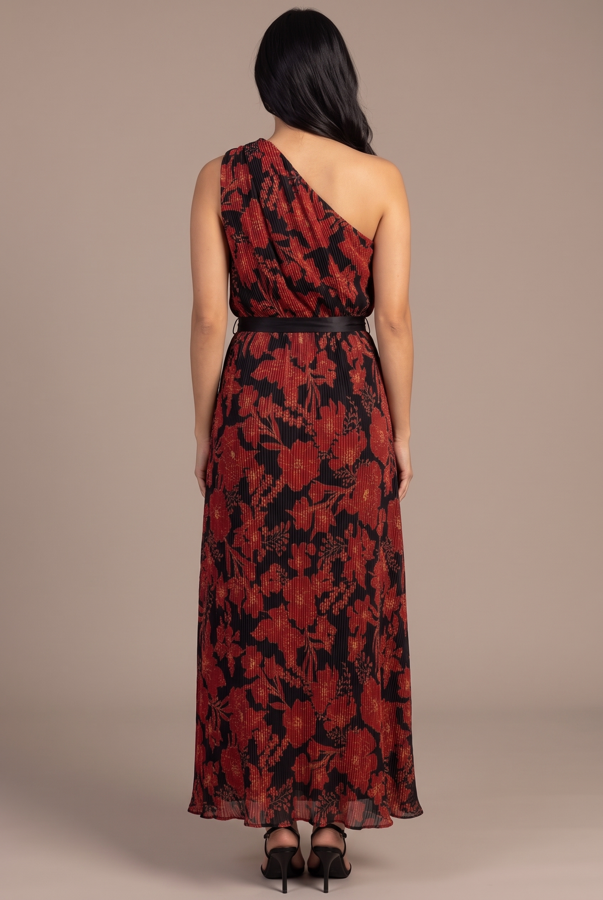 Back of the floral pleated one-shoulder maxi dress showing the strap over her left shoulder and the plain sash band across the back.
