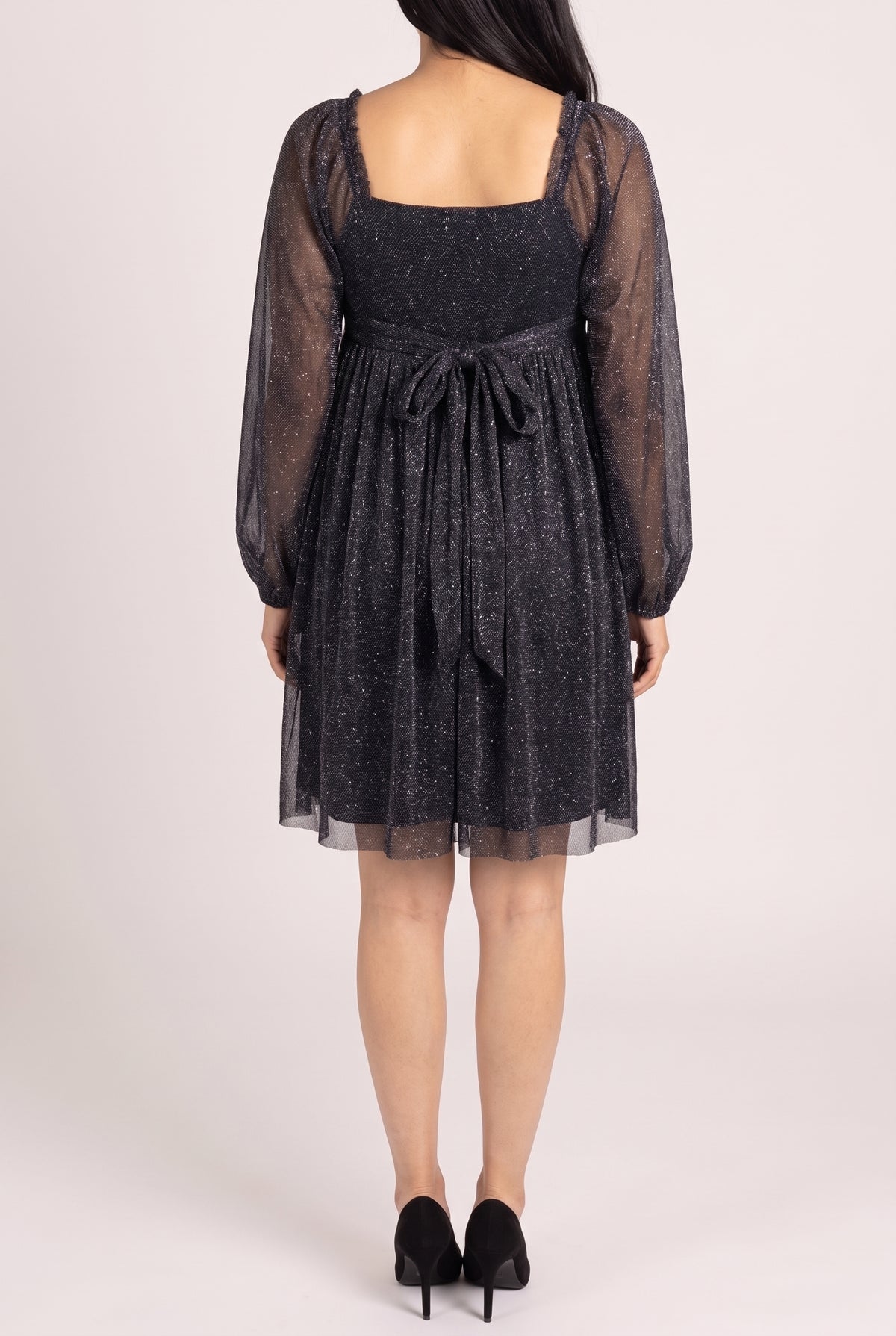 Back view of the black glitter babydoll dress showing the square back, self tie bow at the back waist, sheer sleeves and above the knee hem.