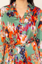 Close-up of the satin sheen, painterly orange, red, purple and navy print on green, the V neckline and the knotted tie belt.