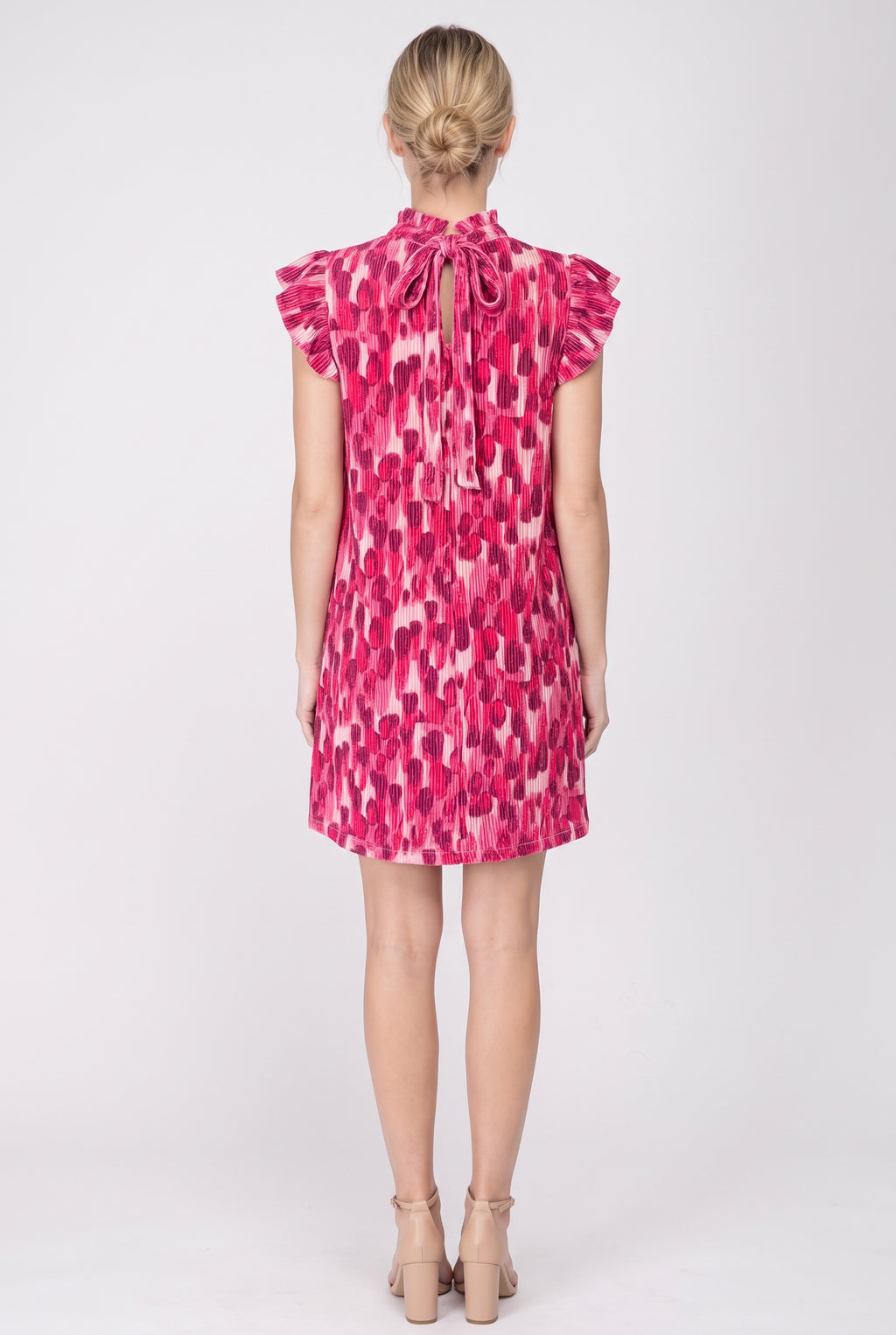 Back view of the pink pleated print shift dress showing the keyhole and tie at the back neck, flutter sleeves and plain hem above the knee.
