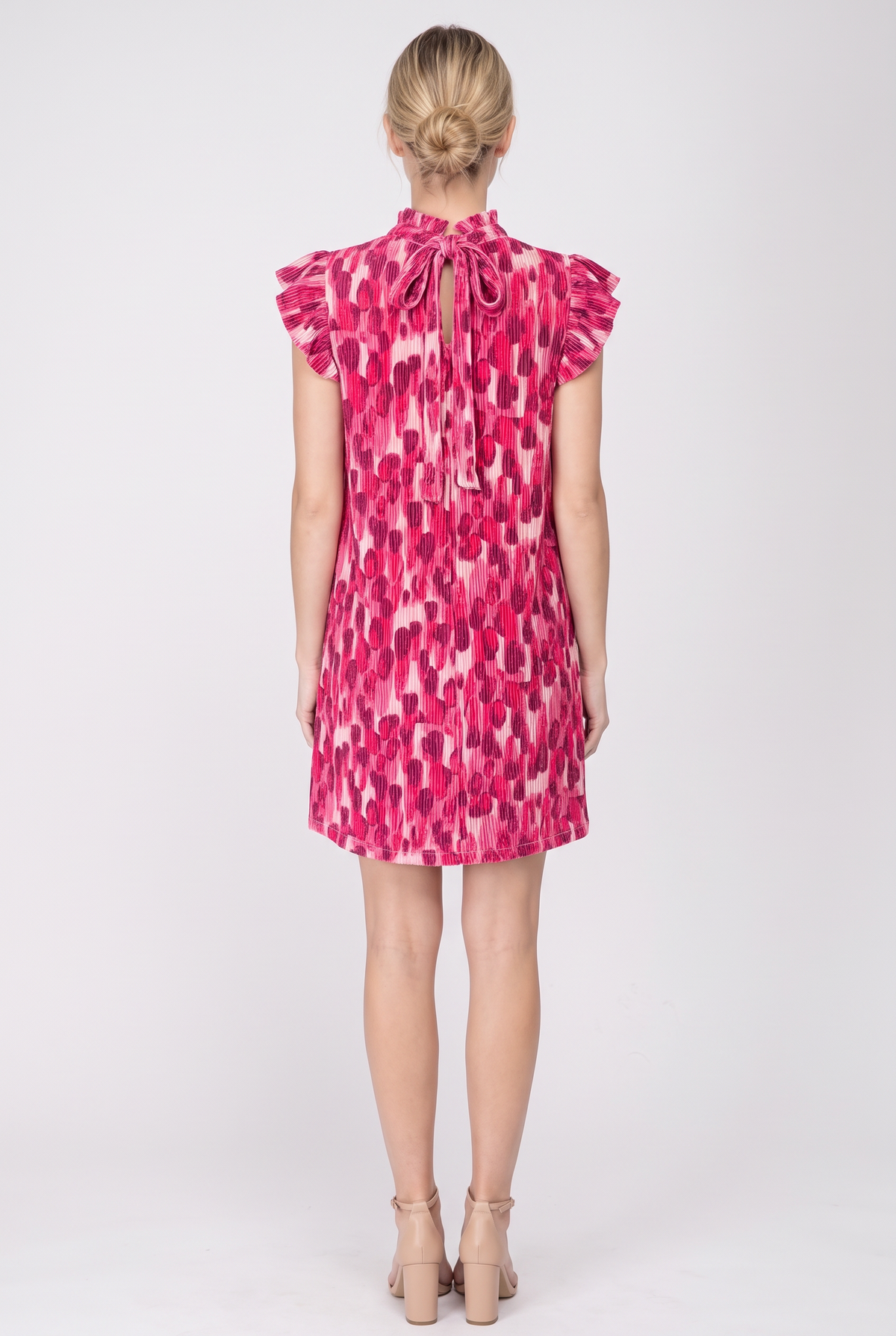 Back view of the pink pleated print shift dress showing the keyhole and tie at the back neck, flutter sleeves and plain hem above the knee.
