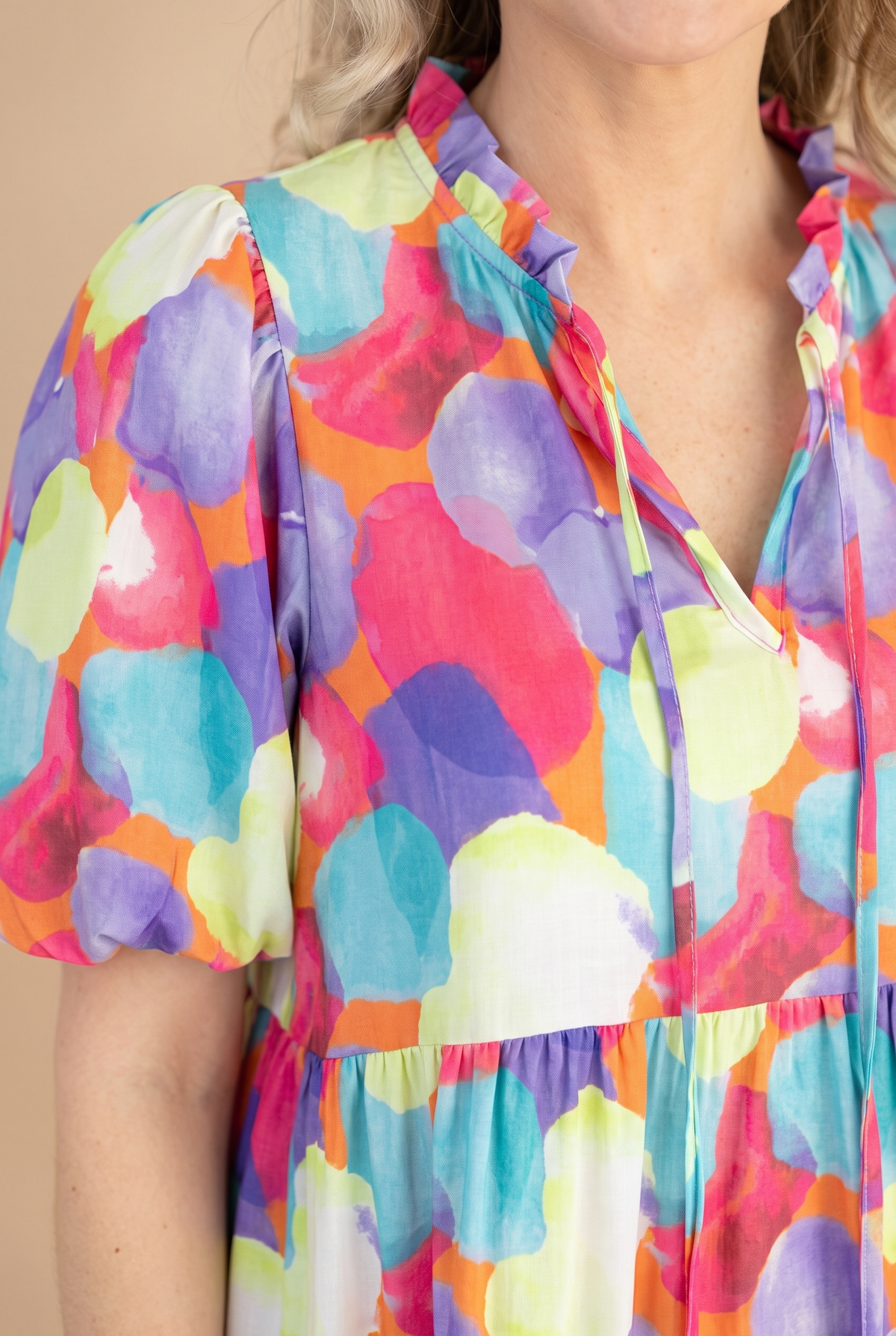 Close detail of the ruffled split neckline with ties, puff sleeve and watercolor dot print.