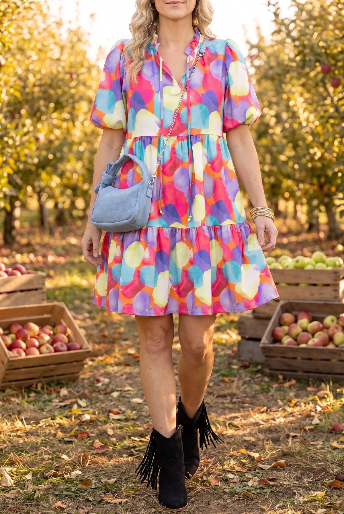 Watercolor print babydoll dress worn with black fringe western ankle boots, a denim crossbody and a gold bangle stack in an autumn apple orchard.