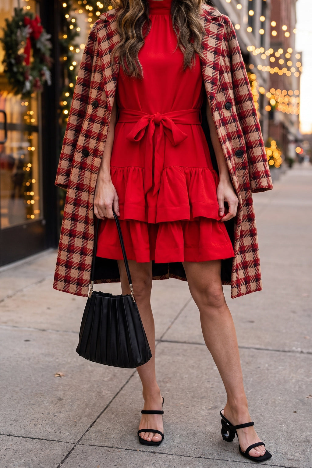 Red ruffle tiered mini dress styled for the holidays with a red houndstooth plaid coat over the shoulders, a black pleated shoulder bag and black sculptural-heel slide sandals