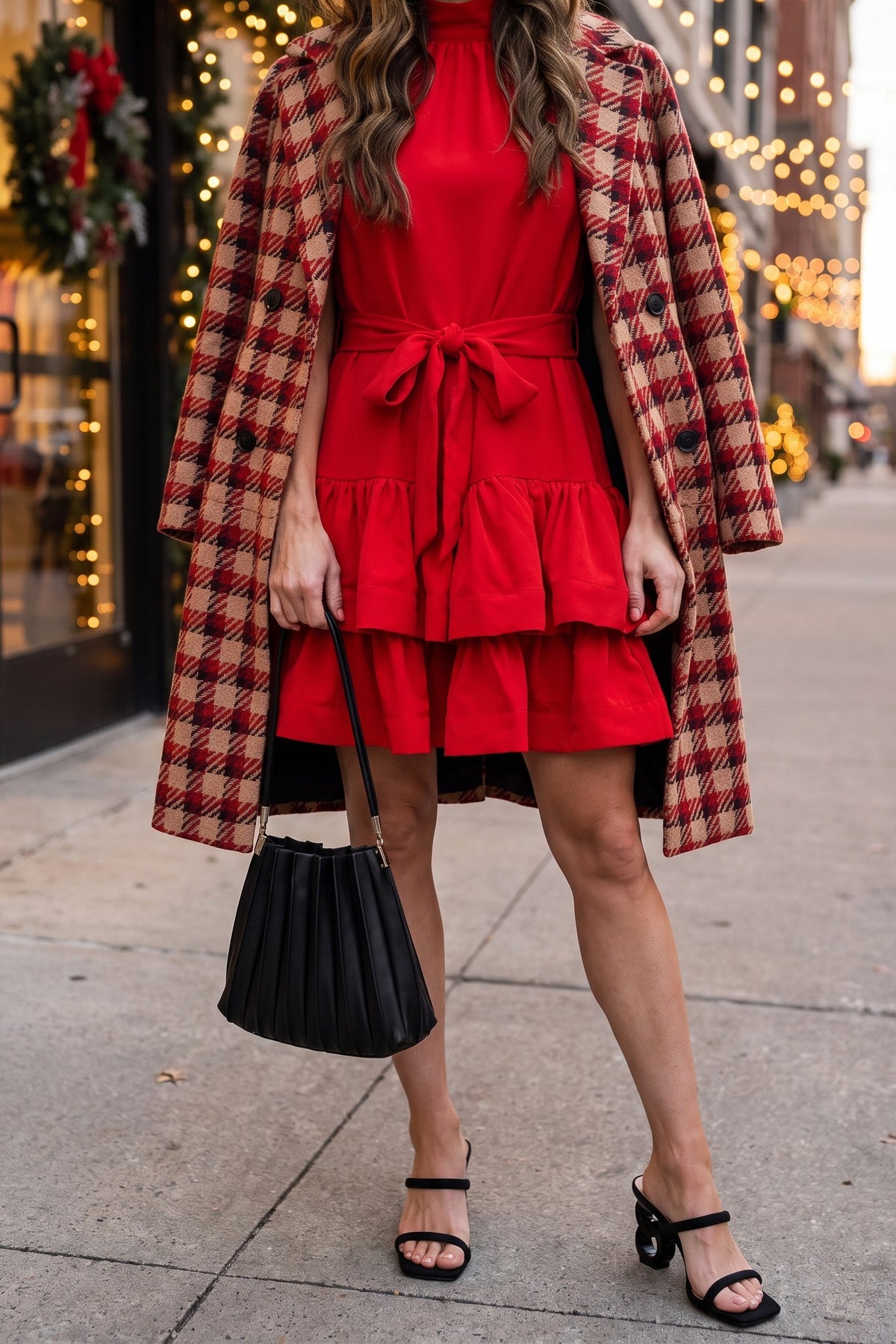 Red ruffle tiered mini dress styled for the holidays with a red houndstooth plaid coat over the shoulders, a black pleated shoulder bag and black sculptural-heel slide sandals