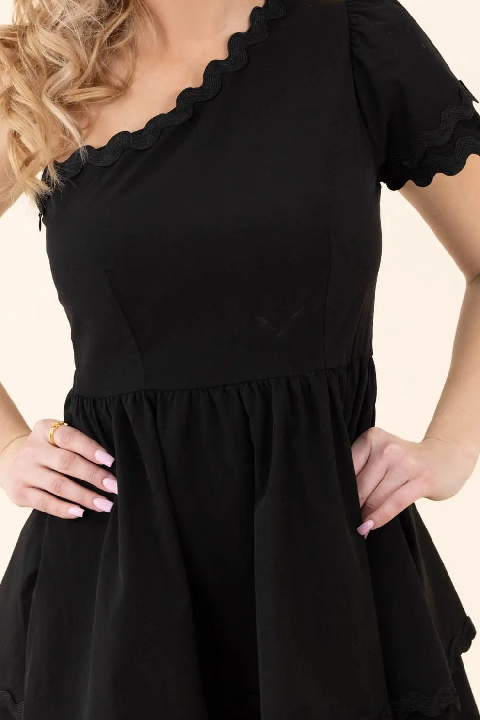 Close-up of the scalloped neckline trim, scalloped puff sleeve and gathered waist of the black mini dress