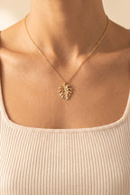 Marina Palm Leaf Necklace worn at true size: a small gold monstera leaf pendant on a fine chain, just below the collarbones