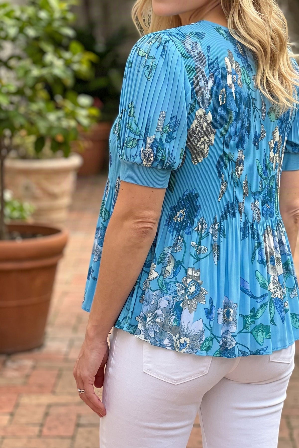 Model wearing the blue floral V-neck pleated top, angled view from the chin down