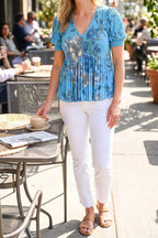 Model wearing the blue floral V-neck pleated top at a cafe, from the chin down
