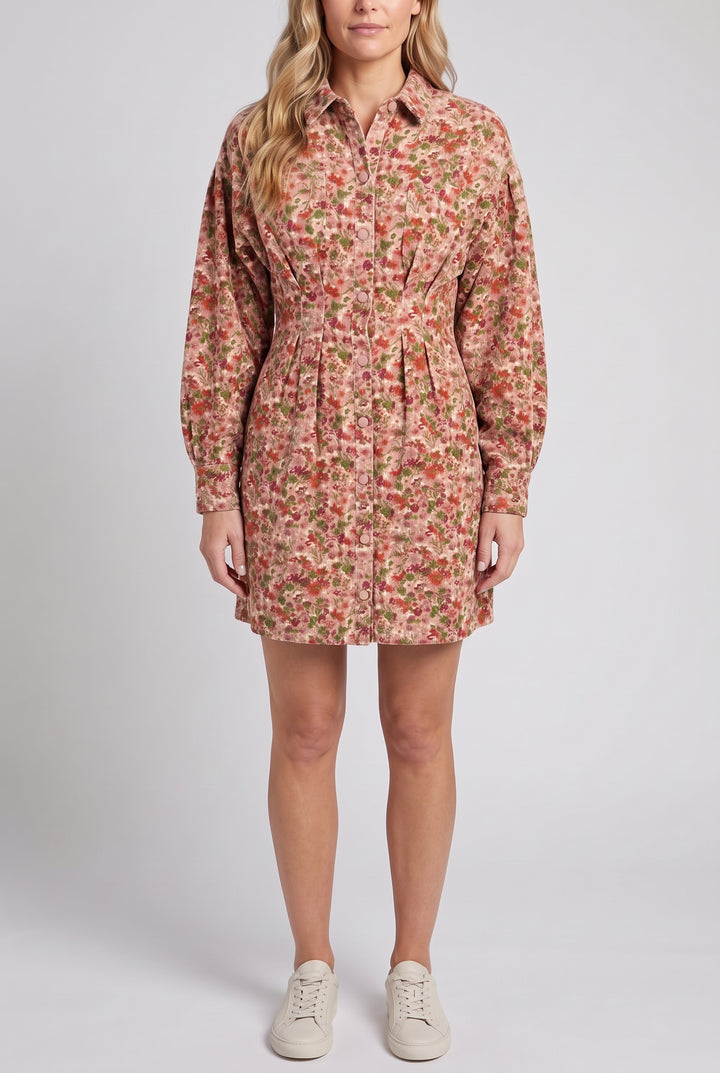 Model wearing the floral corduroy long-sleeve mini dress with cream sneakers, standing against a light grey studio backdrop, cropped below the nose