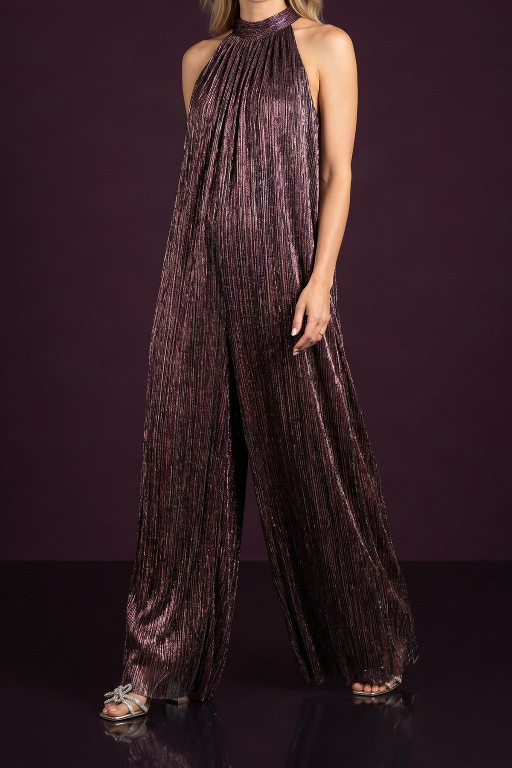 Model wearing the metallic plum halter-neck jumpsuit mid-step, from the chin down