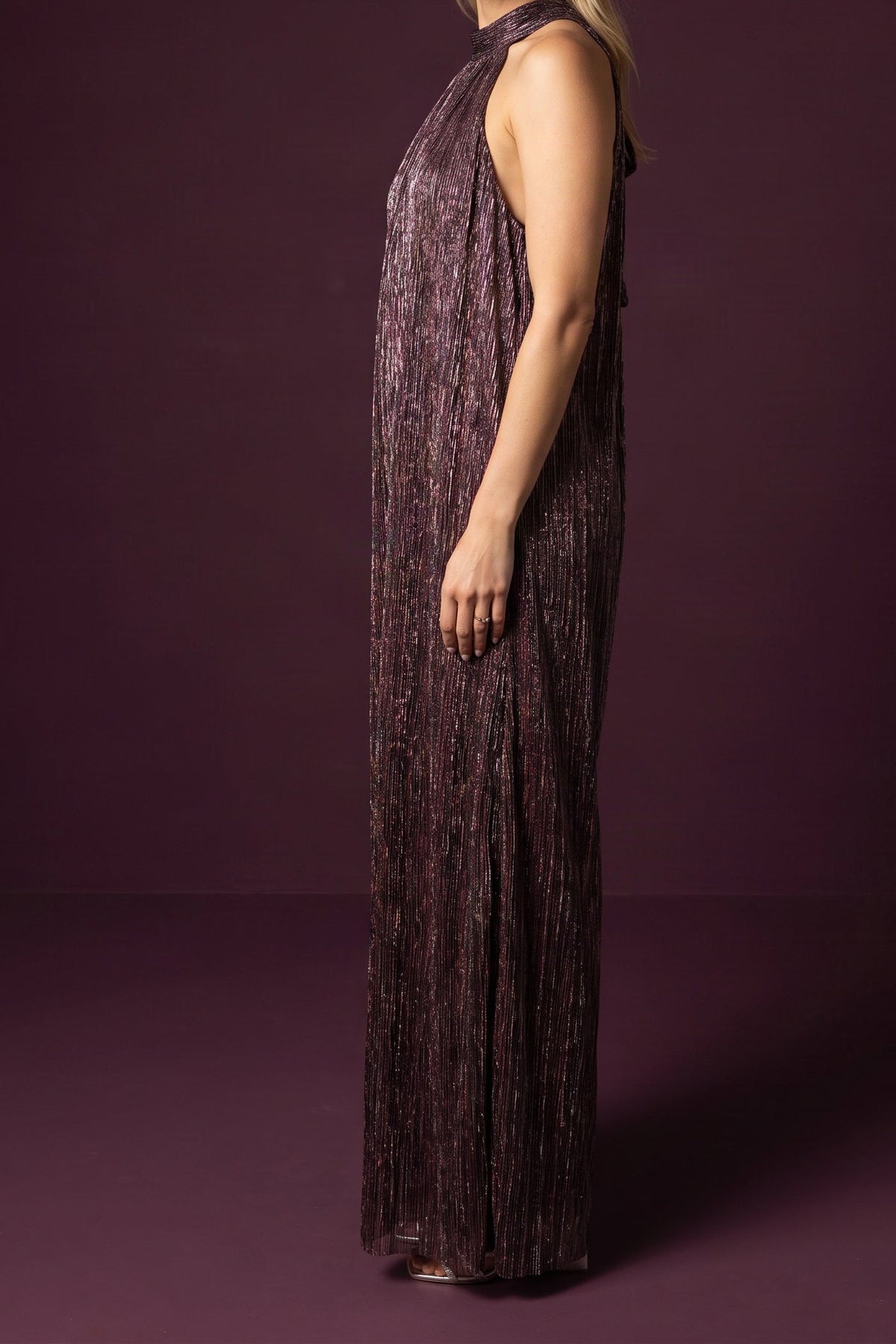 Model wearing the metallic plum halter-neck jumpsuit, side view from the chin down