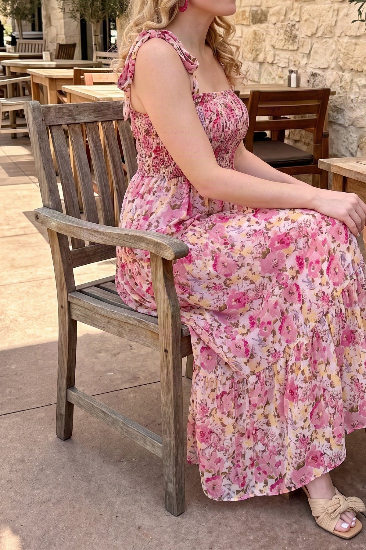 Model wearing the pink floral smocked maxi dress, seated on a bench, from the chin down