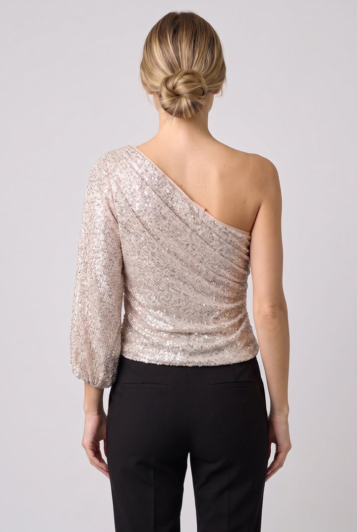 One-shoulder sequin top worn with black trousers, back view on a light-grey studio backdrop