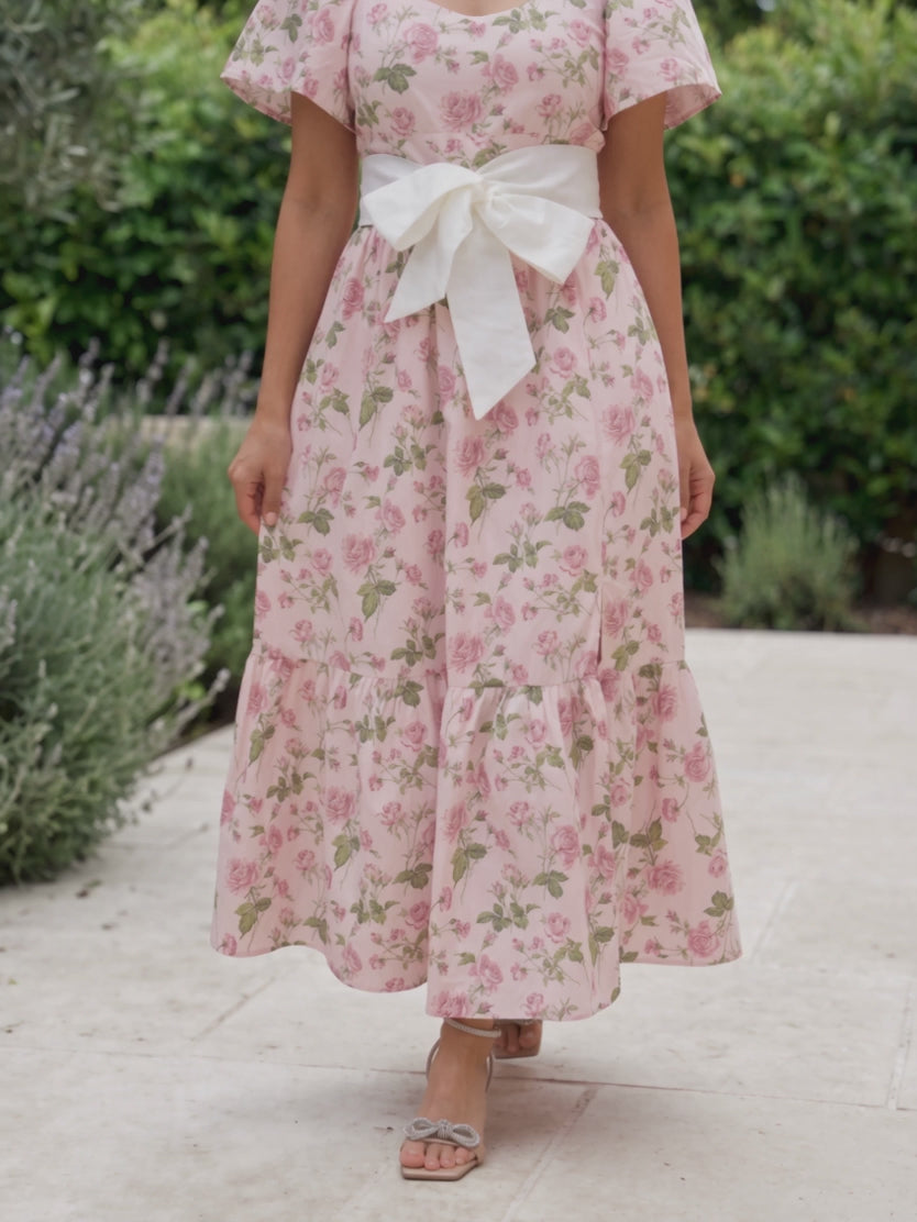 Shweta walking in the Small pink floral dress as its tiered skirt and flutter sleeves move.
