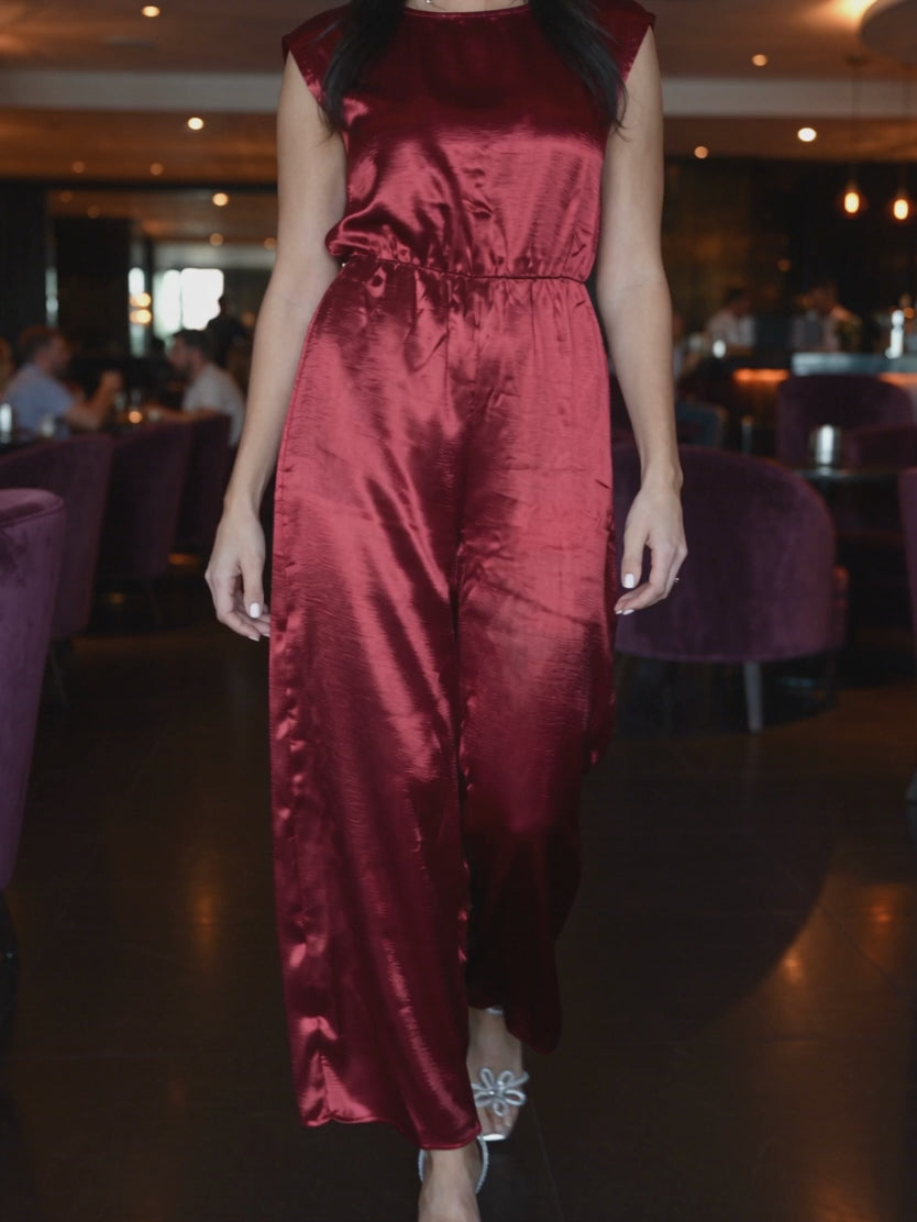 I'm Yours red satin jumpsuit in motion, showing the wide legs and glossy fabric while walking.